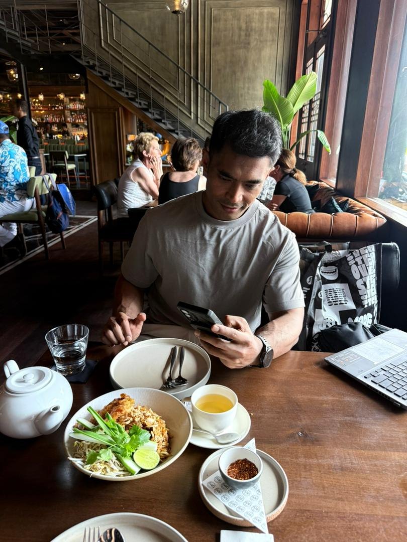 Riz at a cafe table with food, laptop, and phone
